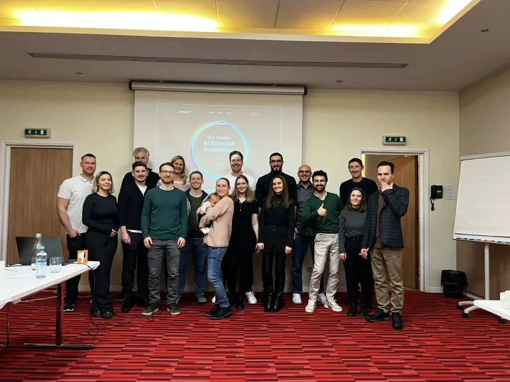 The ExtensityAI team gathered in a meeting room in front of a slide reading "Our mission: AI Research Automation".